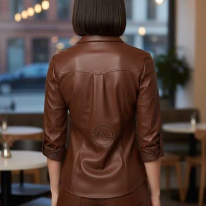 May include: A brown leather jacket with three-quarter sleeves and matching pants. The jacket has a collared neckline and a logo on the back. The outfit is a solid, rich brown color.