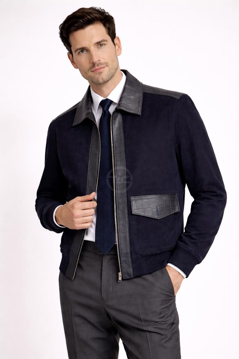 May include: A navy blue suede jacket with black leather detailing on the collar, shoulders, and pockets. The jacket has a front zip and is worn with a white shirt, a navy tie, and grey trousers.