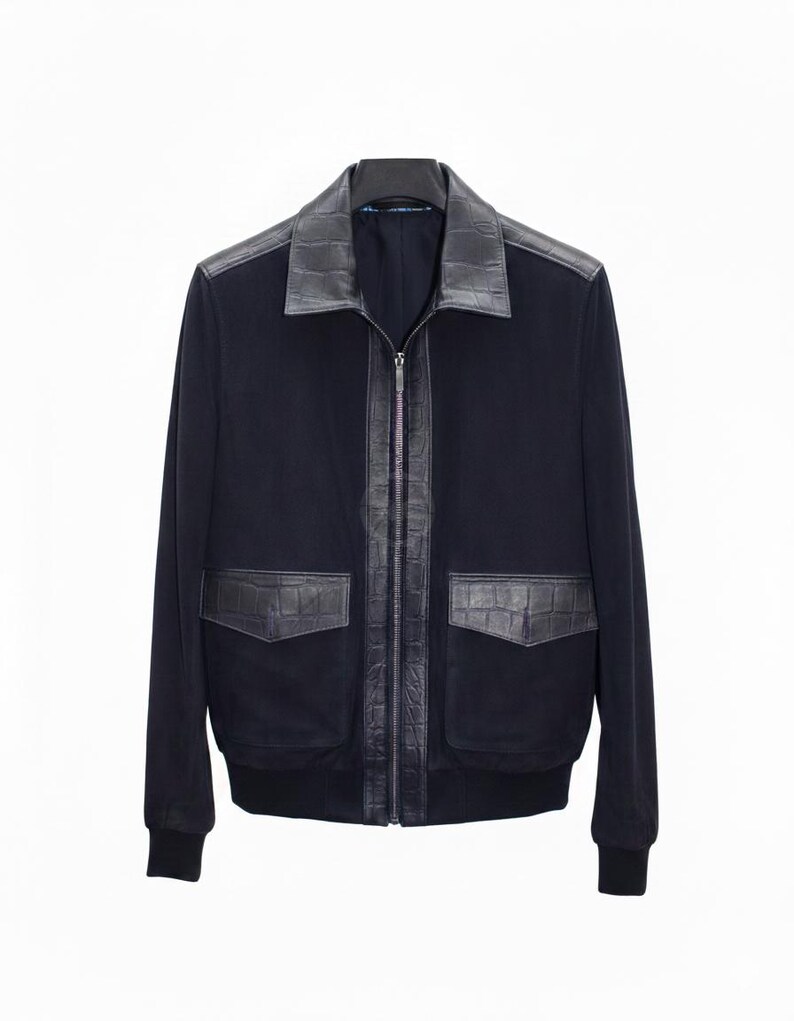 May include: A navy blue bomber jacket with black leather detailing. The jacket has a black leather collar, a zip closure, and two front pockets with leather detailing. The cuffs and hem are ribbed.