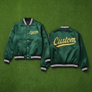 May include: Two green satin bomber jackets with the word "Custom" in gold script on the front and back. The jackets have black and white striped cuffs, collar, and hem. The jackets are button-up.