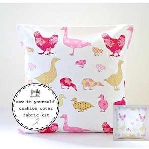 May include: Cushion cover featuring a pattern of pink and yellow chickens, ducks, and geese on a white background. The birds have floral and polka dot patterns. The text "sew it yourself cushion cover fabric kit" is on a circular label.