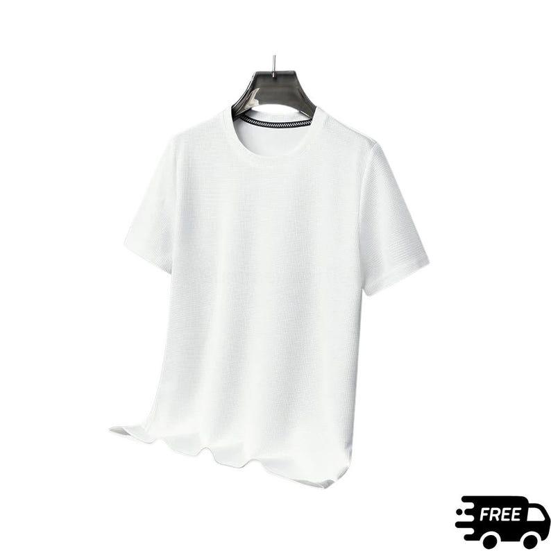 May include: A white, short-sleeved t-shirt with a textured surface, hanging on a black hanger. The shirt has a crew neck and a slightly ruffled hemline. The background is plain white.