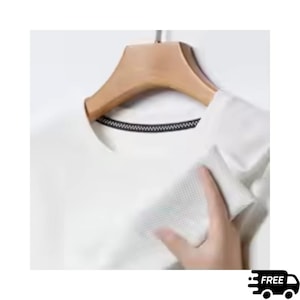 May include: A white, short-sleeved shirt with a textured pattern, hanging on a wooden hanger. The shirt has a black trim around the neckline. A hand is touching the shirt.