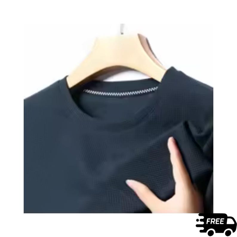 May include: A dark navy blue crew neck shirt with a textured pattern. The shirt is hanging on a wooden hanger. The neckline has a white stitched detail. The image includes a hand touching the shirt. The image also includes the text "FREE" and a graphic of a truck.