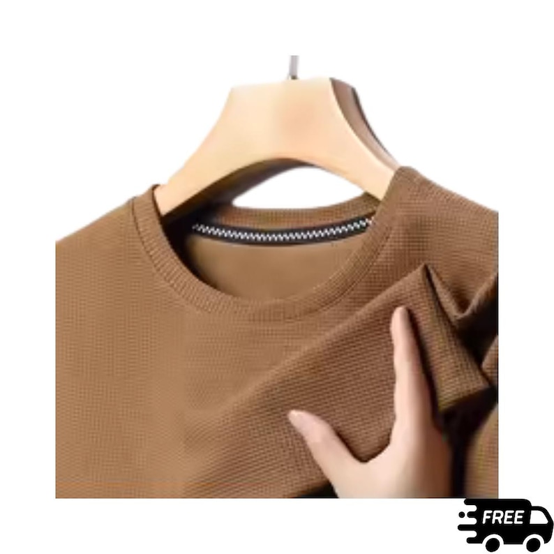 May include: A brown crew neck long-sleeve shirt with a textured waffle knit pattern. The shirt is hanging on a wooden hanger. The collar has a black and white striped trim.