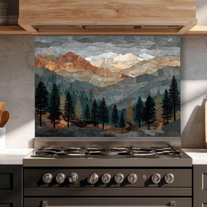 Pode incluir: Um painel de revestimento de cozinha com uma ilustração de paisagem em estilo mosaico de cadeias de montanhas em camadas em tons de cinza, marrom e branco, atrás de uma fileira de pinheiros verde-escuros, sobre um fogão a gás.