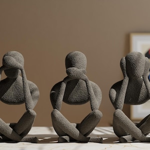 Op de afbeelding: Drie grijze sculpturen die het concept 'Zie geen kwaad, hoor geen kwaad, spreek geen kwaad' uitbeelden. Elke figuur zit met gekruiste benen, handen bedekken ogen, mond en oren. De sculpturen hebben een getextureerd oppervlak.
