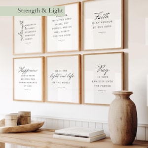 May include: Six framed prints with inspirational quotes in black script on a white background. The prints are in light brown frames. The top left print reads "Strength" and the top right print reads "Faith". A wooden vase and decorative items sit on a wooden table.