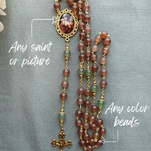 May include: Custom Saint Rosary with brown beads, gold accents, and a detailed cross. The rosary features a central medallion with an image and green beads. The text "Any saint or picture" and "Any color beads" are also visible.