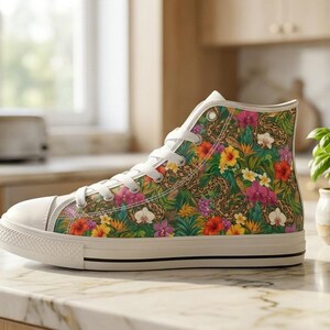 Puede incluir: Una zapatilla de ca&ntilde;a alta con un vibrante estampado tropical de hojas verdes, flores de hibisco rosas y amarillas, y orqu&iacute;deas blancas. El calzado tiene una puntera de goma blanca, cordones blancos y una suela de goma blanca con una raya negra.