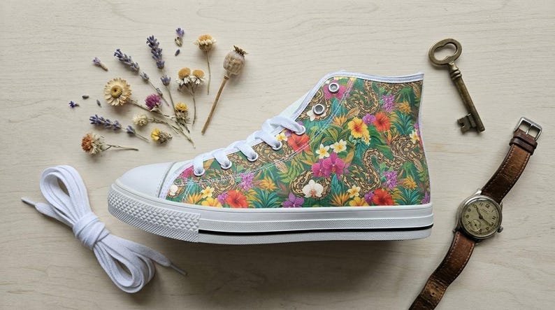 Puede incluir: Una zapatilla de ca&ntilde;a alta con un vibrante estampado floral tropical de hojas verdes, orqu&iacute;deas rosas y flores de hibisco amarillas. El calzado tiene una puntera de goma blanca, cordones blancos y una suela blanca con una fina raya negra lateral.