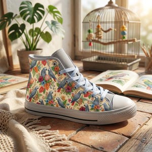 May include: A high-top sneaker featuring a cream-colored canvas upper with a repeating pattern of grey parrots, red flowers, and green foliage. The shoe includes light grey laces, a matching grey tongue, and a white rubber toe cap and sole.