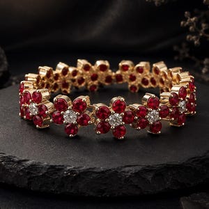 May include: A gold-toned bracelet featuring a repeating floral pattern. Each flower is composed of five deep red circular stones surrounding a single clear, brilliant-cut stone at the centre. The bracelet is constructed from linked segments.