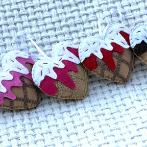 May include: A collection of heart-shaped ornaments resembling ice cream cones. Each ornament features a brown cone with a waffle pattern, topped with white "ice cream" and colorful sprinkles. The "ice cream" comes in shades of pink, red, and brown.