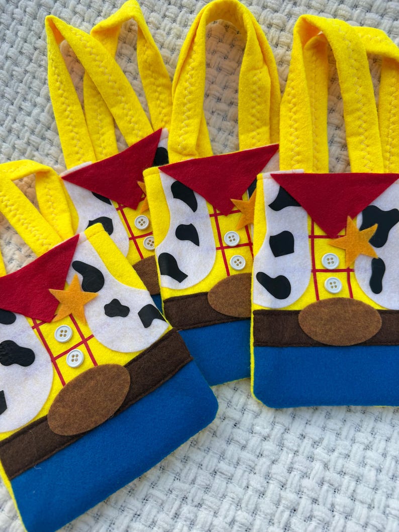 Puede incluir: Una colecci&oacute;n de bolsas de fieltro amarillas, azules, rojas y blancas. Las bolsas est&aacute;n dise&ntilde;adas para parecerse a un personaje de dibujos animados, con una camisa amarilla, pantalones azules, un pa&ntilde;uelo rojo y un cintur&oacute;n marr&oacute;n. Cada bolsa tiene un asa amarilla y una insignia en forma de estrella.