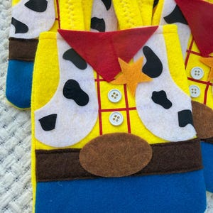 Puede incluir: Bolsas de fieltro amarillas con un dise&ntilde;o inspirado en un personaje de vaquero. Las bolsas presentan un pa&ntilde;uelo rojo, detalles blancos con manchas negras, cintur&oacute;n marr&oacute;n y una insignia en forma de estrella. Se utiliza fieltro azul y amarillo para la base de las bolsas.