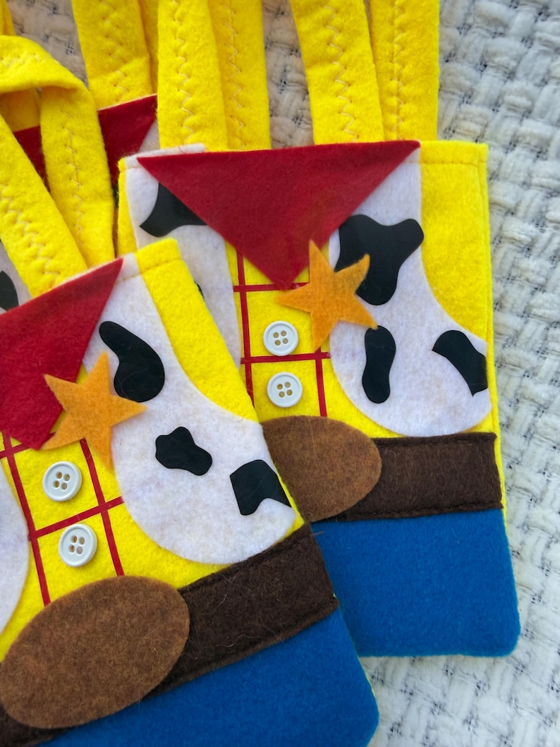 Puede incluir: Calcetines navide&ntilde;os de fieltro amarillo con tem&aacute;tica de Woody de Toy Story. Los calcetines tienen un tri&aacute;ngulo rojo, estampado de vaca blanco y negro, detalles de fieltro marr&oacute;n y fondos de fieltro azul. Cada calcet&iacute;n tiene una estrella y detalles de botones.