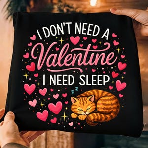 May include: Black pillow with the text "I DON'T NEED A Valentine I NEED SLEEP" in white and pink. The pillow features pink hearts and a cartoon orange tabby cat curled up asleep. A fun Valentine's Day or cat lover's gift.