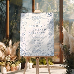Könnte beinhalten: Eine hölzerne Staffelei zeigt ein Schild mit dem Text "The Summer I Turned Thirteen Welcome to Sarah's Birthday Party". Das Schild hat einen weißen Hintergrund mit blauen Muschel- und Schleifenillustrationen. Die Staffelei steht in einem Raum mit Pflanzen.