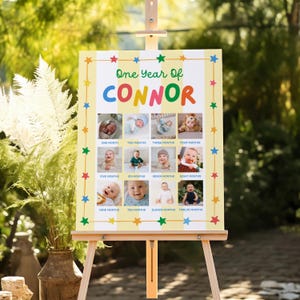 May include: A rectangular milestone sign featuring the text One Year Of CONNOR in colorful letters, surrounded by a border of small stars. The sign displays twelve individual photographs of a baby, each labeled with a month from one to twelve.