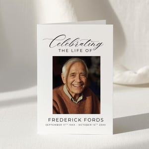 May include: A white memorial card with the words "Celebrating THE LIFE OF" in elegant script. Below is a framed photograph of a smiling older man. The card includes the name "FREDERICK FORDS" and dates.
