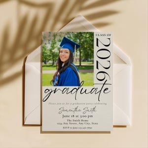 May include: Graduation announcement card featuring a photo of a graduate in a blue cap and gown. The card includes the text "Class of 2026" and "graduate" in a stylish font. Additional text provides party details, including the date, time, and location.
