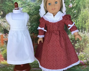 May include: A red and white patterned dress with a white lace trim and a white bonnet. The dress is on a doll stand. A white apron is on a separate doll stand.