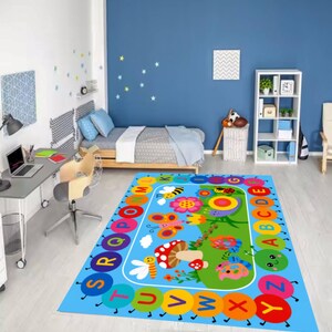 Pode incluir: Um tapete infantil colorido com uma borda de alfabeto e ilustra&ccedil;&otilde;es l&uacute;dicas de insetos, flores e cogumelos. O tapete &eacute; predominantemente azul com uma &aacute;rea central verde e apresenta um design l&uacute;dico para o quarto de uma crian&ccedil;a.