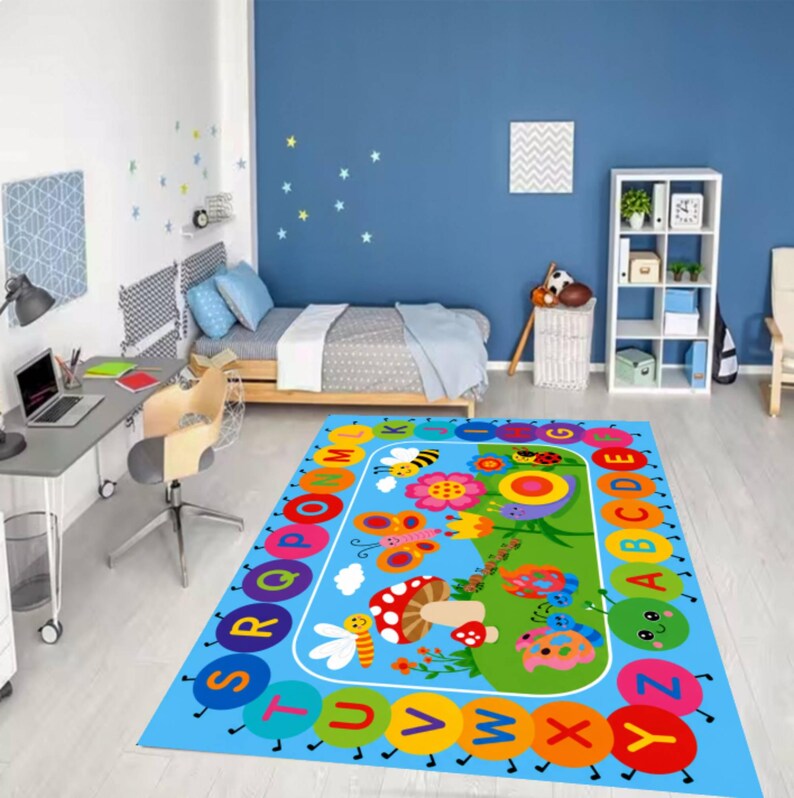 Pode incluir: Um tapete infantil colorido com uma borda de alfabeto e ilustra&ccedil;&otilde;es l&uacute;dicas de insetos, flores e cogumelos. O tapete &eacute; predominantemente azul com uma &aacute;rea central verde e apresenta um design l&uacute;dico para o quarto de uma crian&ccedil;a.