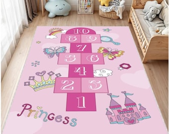 May include: Pink hopscotch rug with a princess theme. The rug features a hopscotch grid with numbers, butterflies, a rainbow, a crown, and a castle. The word "Princess" is written in cursive.
