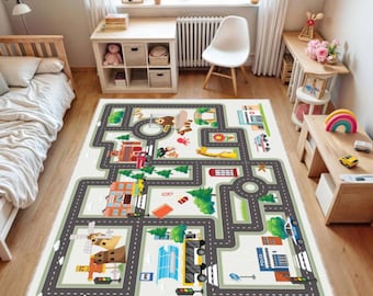 May include: A large, rectangular play rug with a road map design. The rug features gray roads, colorful buildings, trees, and vehicles. The rug is on a hardwood floor in a child's bedroom, with a bed, desk, and other furniture visible in the background.