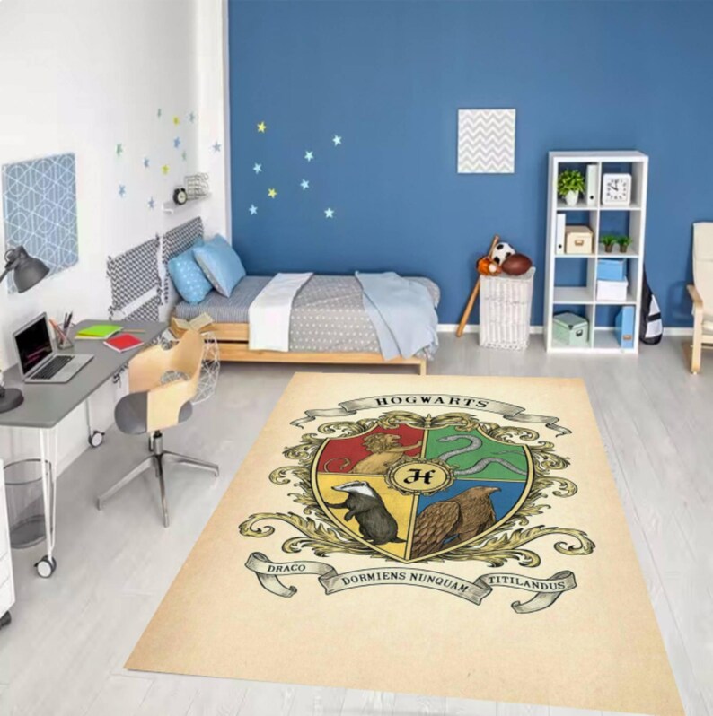 May include: A rectangular rug featuring the Hogwarts crest, with the school's name at the top and the motto "Draco Dormiens Nunquam Titillandus" at the bottom. The crest is divided into four sections, each with a different animal and color.