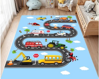 Op de afbeelding: Blauw kinderspeelkleed met een wegontwerp en diverse voertuigen. Het kleed bevat een brandweerwagen, een ambulance, een politieauto, een schoolbus, een tractor en andere voertuigen. Witte wolken en bomen zijn ook afgebeeld.