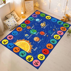 May include: A rectangular blue educational rug featuring a solar system design with planets and the sun. The rug has a border with the alphabet in colorful circles. The rug is designed for children.