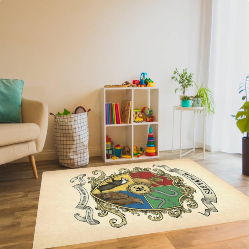 May include: A rectangular beige rug featuring the Hogwarts crest. The crest is a colorful emblem with a shield design, including a lion, eagle, badger, and snake. The rug is placed in a room with a white bookshelf and toys.