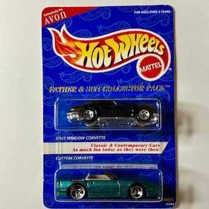 May include: A Hot Wheels Father & Son Collector Pack featuring two toy Corvettes. The top car is a black Split Window Corvette, and the bottom is a Custom Corvette in teal. The packaging is blue with the Hot Wheels logo and Avon branding.