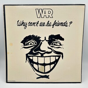 May include: A square vinyl record album cover with a cream background. The text WAR and Why can't we be friends? appear in black. A bold black ink illustration of a wide, grinning face with a single gold-colored tooth is centered below.