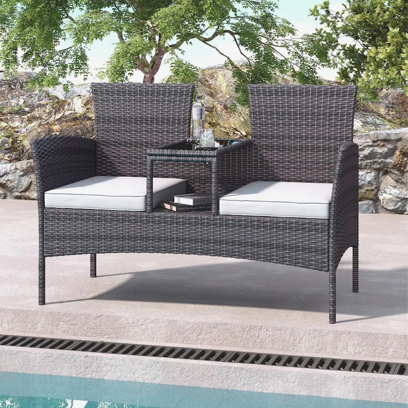 Puede incluir: Un sof&aacute; de mimbre gris oscuro con una peque&ntilde;a mesa entre los asientos. El sof&aacute; tiene cojines blancos y est&aacute; colocado cerca de una piscina. Una botella y vasos est&aacute;n sobre la mesa. El sof&aacute; est&aacute; dise&ntilde;ado para uso en exteriores.