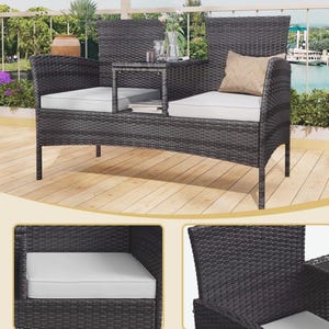 Puede incluir: Sof&aacute; de exterior de mimbre gris oscuro con una mesa auxiliar incorporada. El sof&aacute; tiene dos asientos con cojines blancos y un peque&ntilde;o coj&iacute;n beige. La mesa auxiliar est&aacute; entre los asientos. El sof&aacute; est&aacute; sobre una terraza de madera.