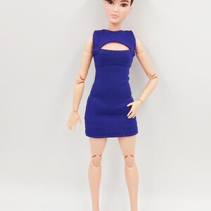 May include: A fashion doll in a royal blue mini-dress with a keyhole detail. The doll has short, dark hair and is wearing purple high-heeled shoes. The doll is set against a plain white backdrop.