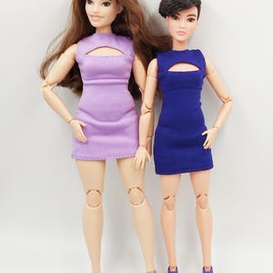 May include: Two fashion dolls in dresses. One doll wears lavender, the other blue. Both dolls have matching heels. The dolls stand against a white backdrop. The dresses have a keyhole design.