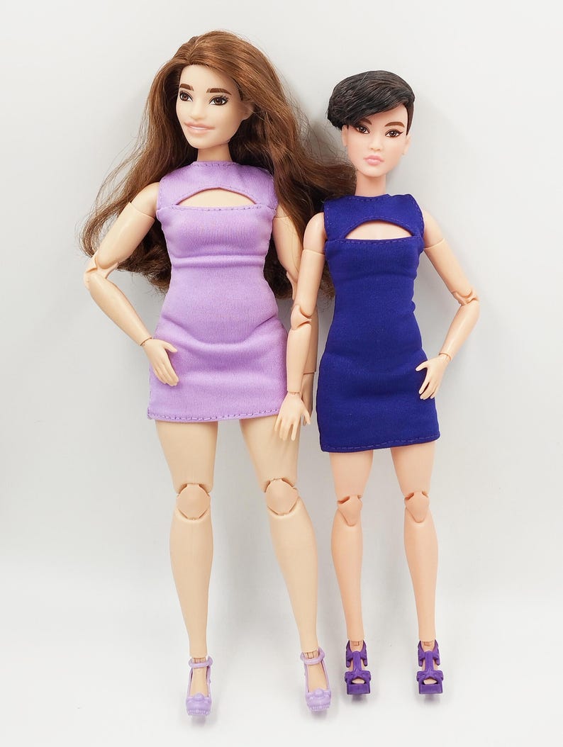 May include: Two fashion dolls in dresses. One doll wears lavender, the other blue. Both dolls have matching heels. The dolls stand against a white backdrop. The dresses have a keyhole design.