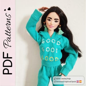 Pode incluir: Uma boneca vestindo um agasalho turquesa com a palavra "GOOD" bordada na frente do moletom com capuz. A boneca tem cabelo longo e preto, brincos dourados e brincos de borla verdes. O texto "PDF Patterns" também está presente.