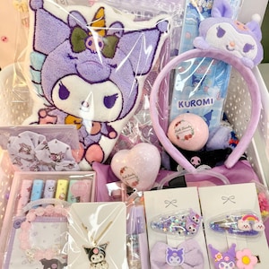Op de afbeelding: Een witte mand gevuld met diverse paarse en roze accessoires. Items zijn onder meer een pluche kussen, haaraccessoires, een ketting, een armband en een hartvormige badbruisbal. De afbeelding toont ook een hoofdband, een bladwijzer en een muntenzak.