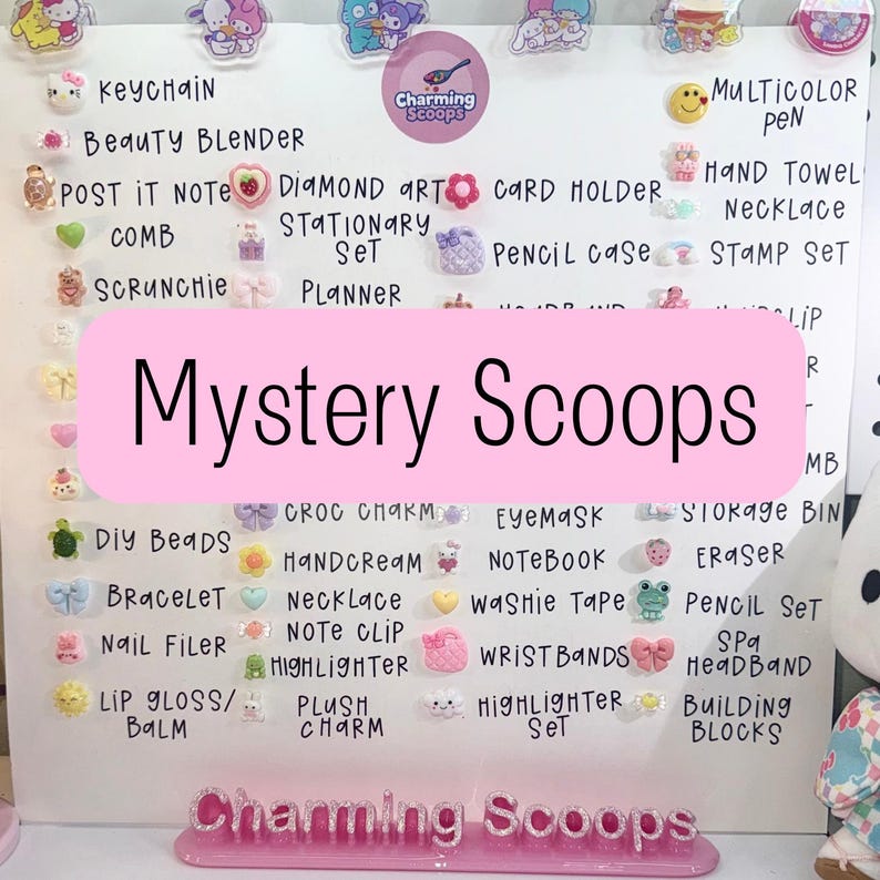 Op de afbeelding: Een wit bord met diverse kleine, kleurrijke accessoires, waaronder sleutelhangers, make-up sponzen en briefpapier. De tekst "Mystery Scoops" is prominent aanwezig. De onderkant van het bord toont "Charming Scoops".