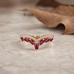 Peut inclure: Une bague en or en forme de chevron ornée d'une rangée de sept rubis rouges taille marquise et d'une fine bande de petits diamants blancs ronds sertis sur le bord supérieur, créant un design en V avec une finition métallique polie.