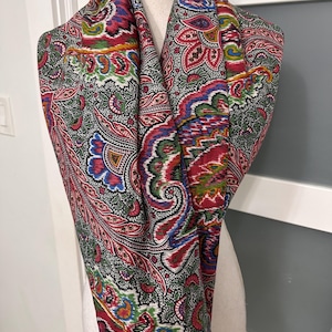 Peut inclure: Écharpe paisley colorée avec un motif vibrant rouge, bleu, vert et blanc. L'écharpe est drapée sur un mannequin, mettant en valeur son design complexe et ses bords frangés. Cet accessoire ajoute une touche bohème.