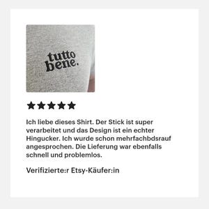 May include: A heather gray t-shirt featuring the black embroidered text "tutto bene." on the chest. The embroidery is positioned on the upper left side of the garment, showcasing a clean, bold, and lowercase serif typeface design.