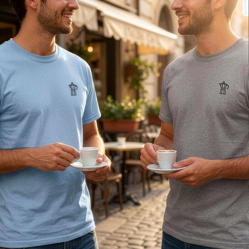 以下が含まれることがあります： ライトブルーのTシャツとグレーの杢Tシャツ。どちらも左胸にモカポットの小さな黒い線画がプリントされています。両方のシャツは半袖でクルーネックのデザインであり、無地の生地で作られています。