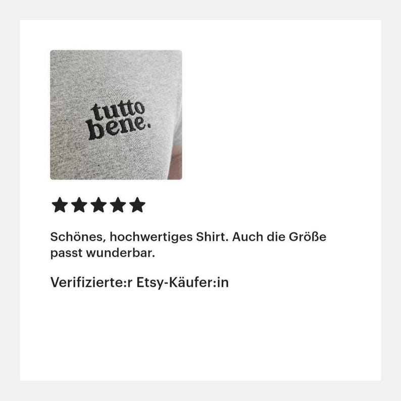 May include: A heather gray t-shirt featuring the black embroidered text "tutto bene." on the chest. The fabric has a visible knit texture, and the lettering is displayed in a lowercase, rounded serif font with a period at the end.